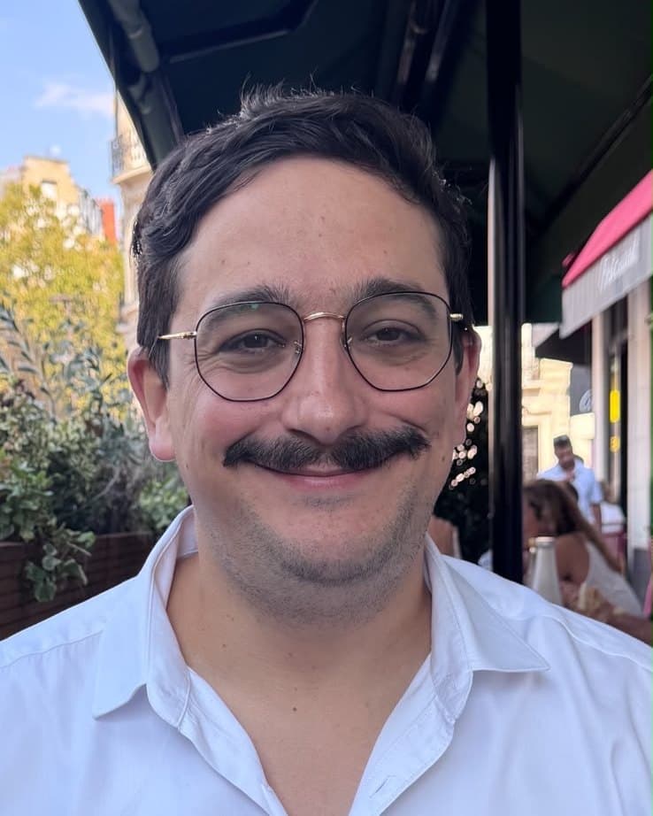 Thomas Linck, concepteur d'Arrive au sec, souriant, en chemise blanche à une terrasse parisienne.
