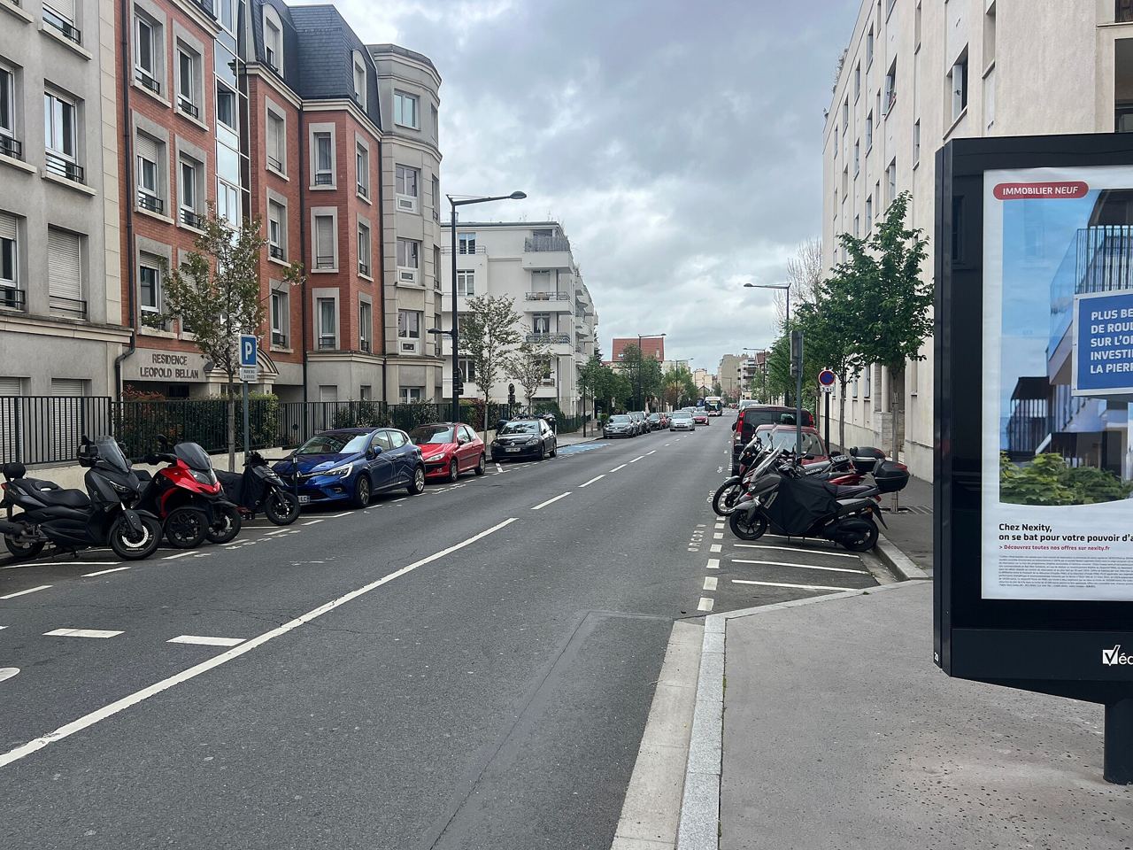 L'avenue Charles-de-Gaulle à Bois-Colombes, large chaussée bordée d'immeubles, avec des scooters et des motos garés sur le côté