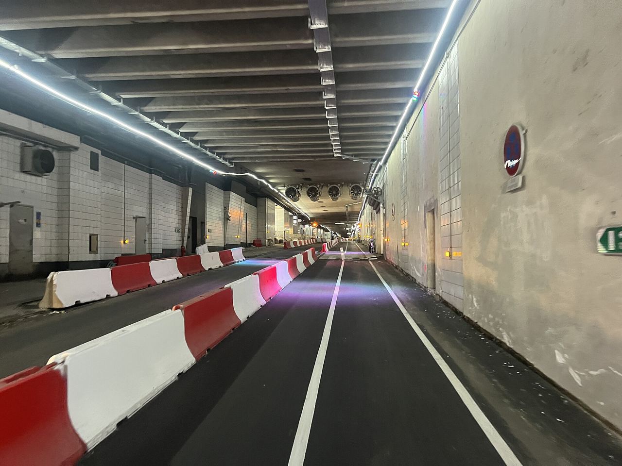 Voie cyclable dans le tunnel de la voie des Bâtisseurs, sous la dalle de La Défense à Courbevoie, séparée des voitures par des blocs rouges et blancs.