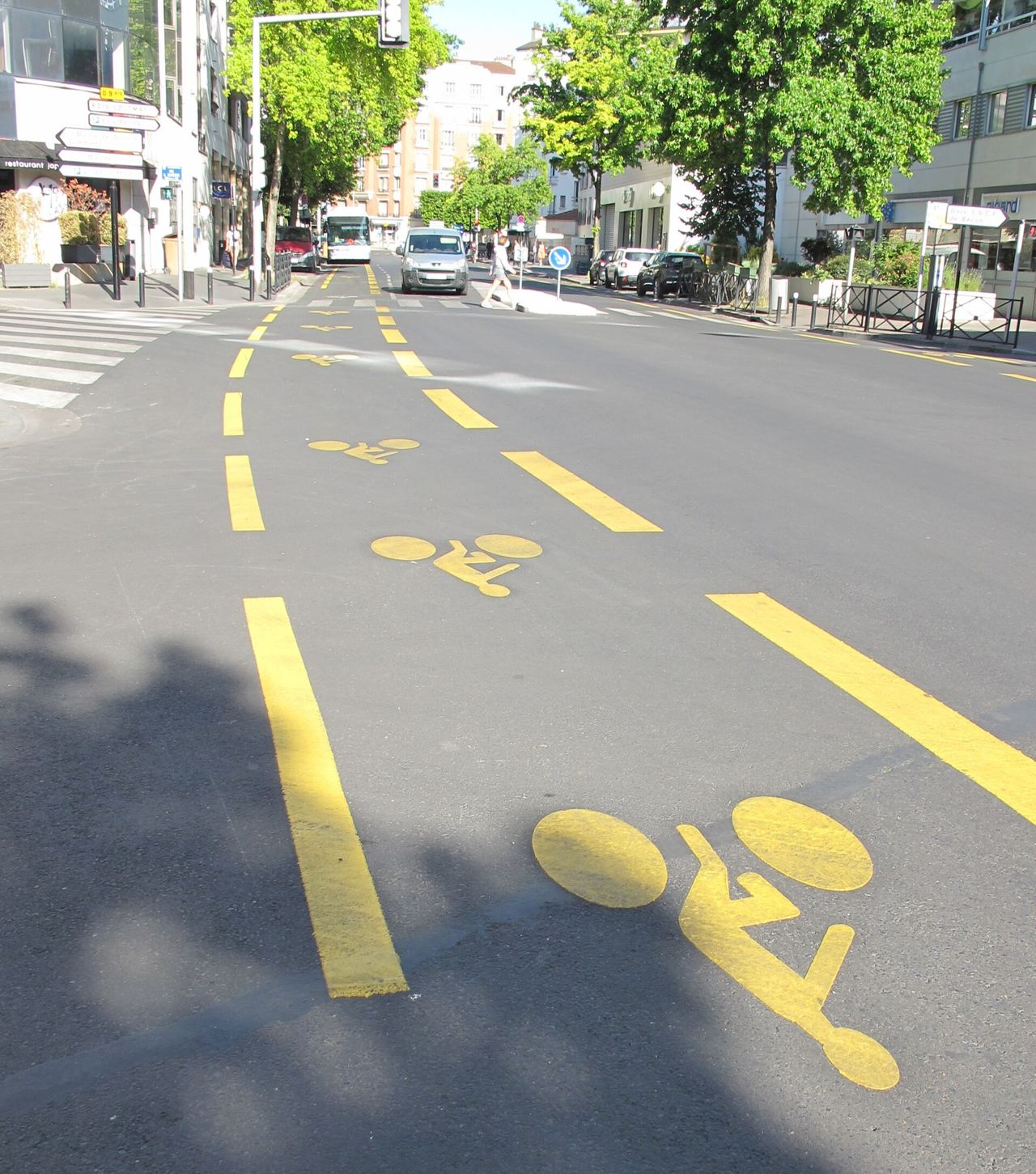 Piste cyclable temporaire tracée en jaune sur la chaussée d'une avenue de Courbevoie en mai 2020, avec pictogrammes vélo.