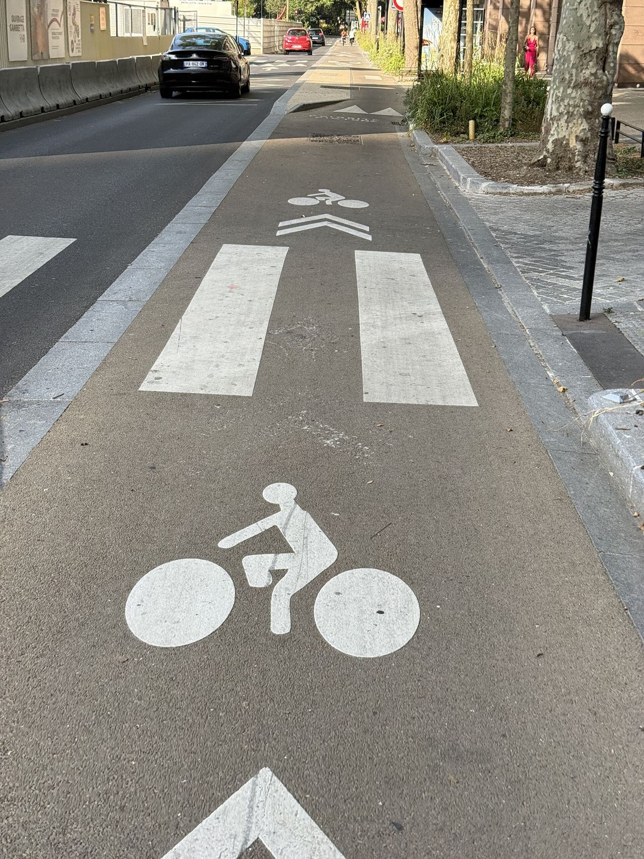 Piste cyclable de l'avenue Gambetta à Courbevoie qui traverse un passage piéton, marquée d'un grand pictogramme vélo et de chevrons blancs, à côté des voitures.