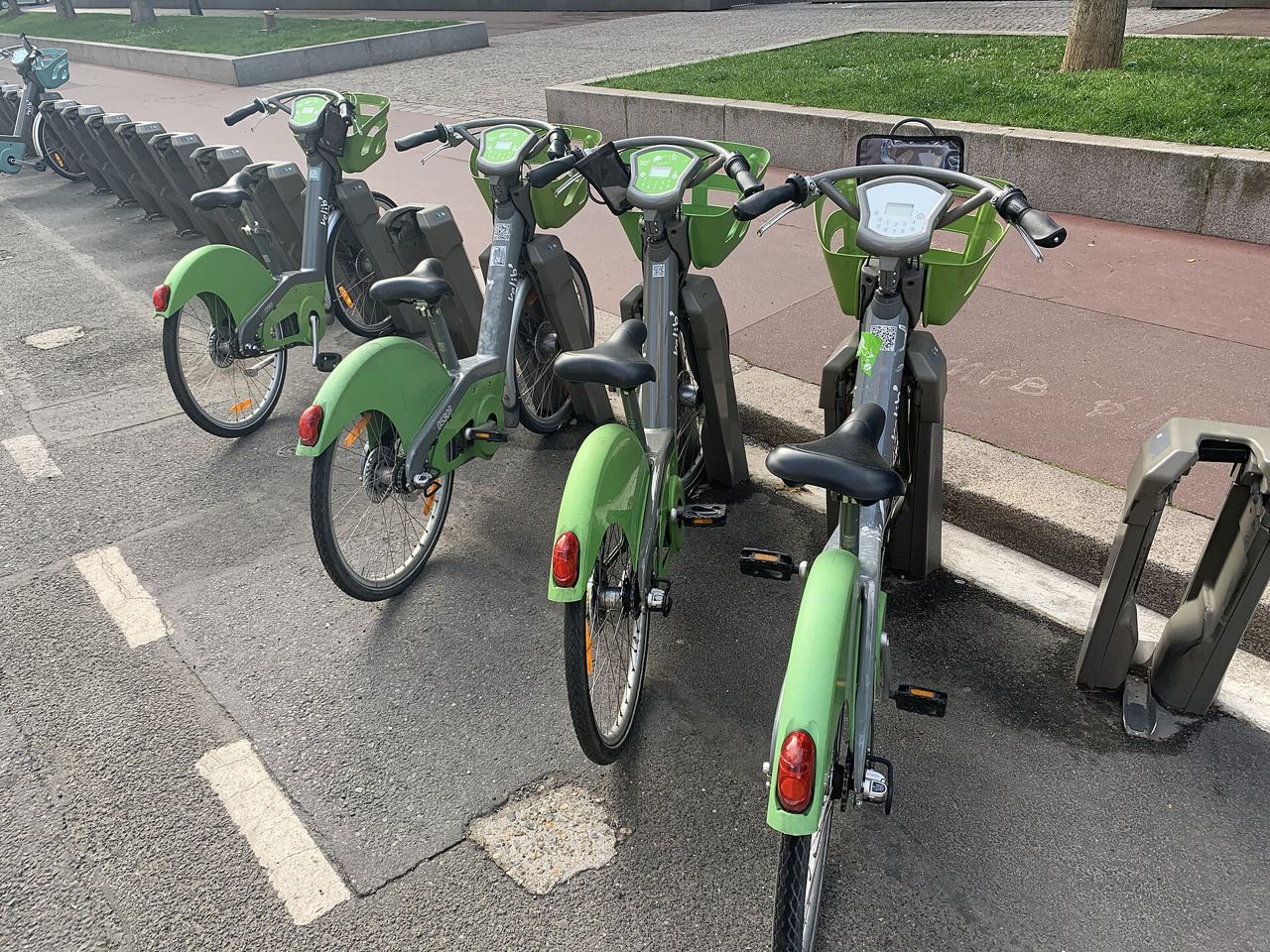 Vélib' verts et électriques alignés à leurs bornes à la station Paul-Vaillant-Couturier – Chaptal de Levallois-Perret, au bord d'une piste rouge.
