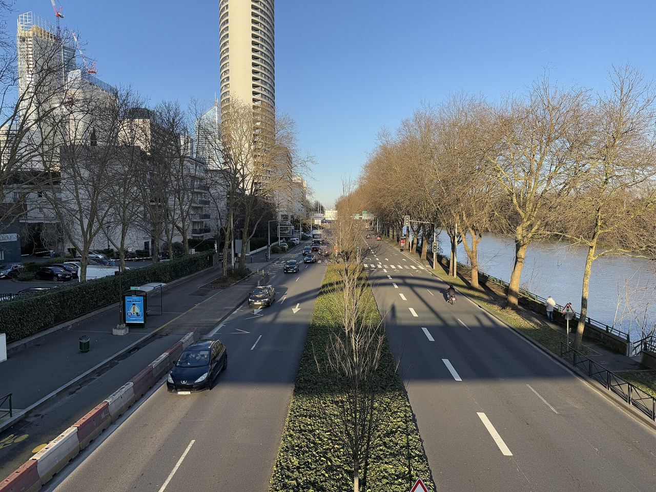 Le quai de Dion-Bouton à Puteaux vu d'une passerelle : deux fois deux voies séparées par un terre-plein planté, la Seine et ses arbres à droite, les tours de La Défense à gauche.