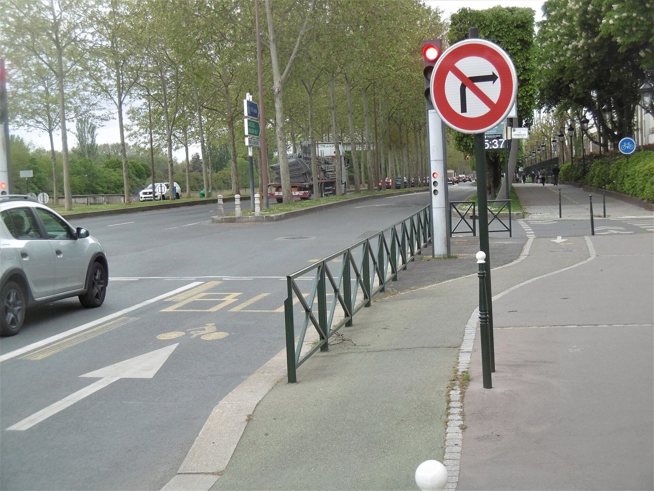 Carrefour sur le quai de Dion-Bouton : pictogramme vélo et flèche peints sur la chaussée, trottoir partagé derrière une barrière verte, panneau d'interdiction de tourner à droite.