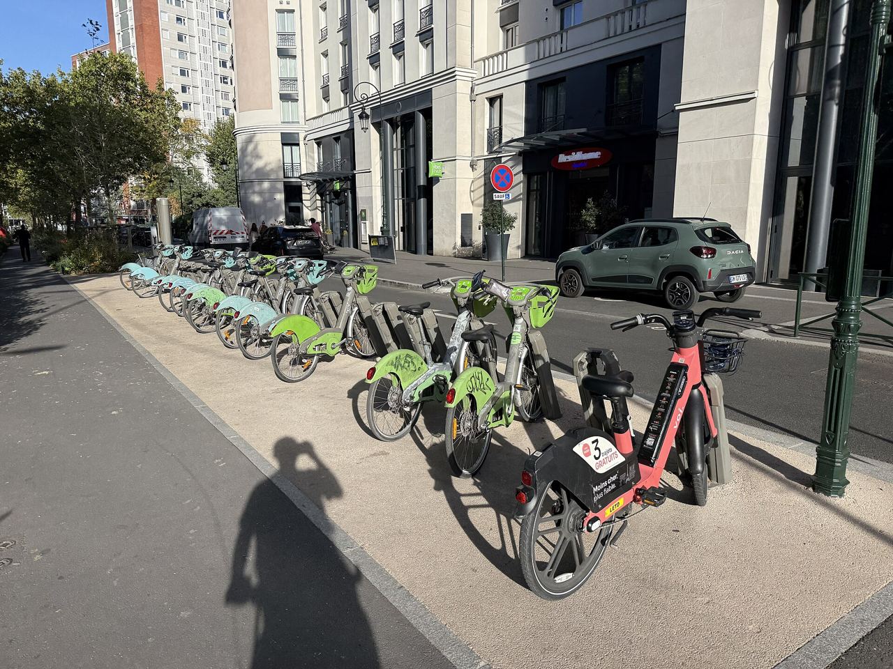 Station Vélib' De Gaulle - Moulin sur l'avenue du Général-de-Gaulle à Puteaux : une rangée de Vélib' verts et bleus à leurs bornettes, au soleil, avec un vélo électrique rouge garé devant.