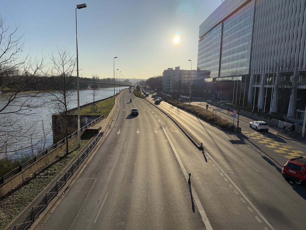 Le quai de Dion-Bouton à contre-jour : la Seine à gauche, la chaussée large et presque vide, et des immeubles de bureaux à droite.
