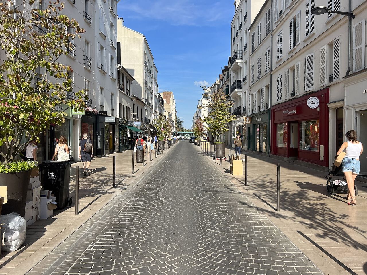 La rue du Midi à Vincennes, pavée et bordée de commerces, avec des piétons sur les trottoirs un soir d'été.